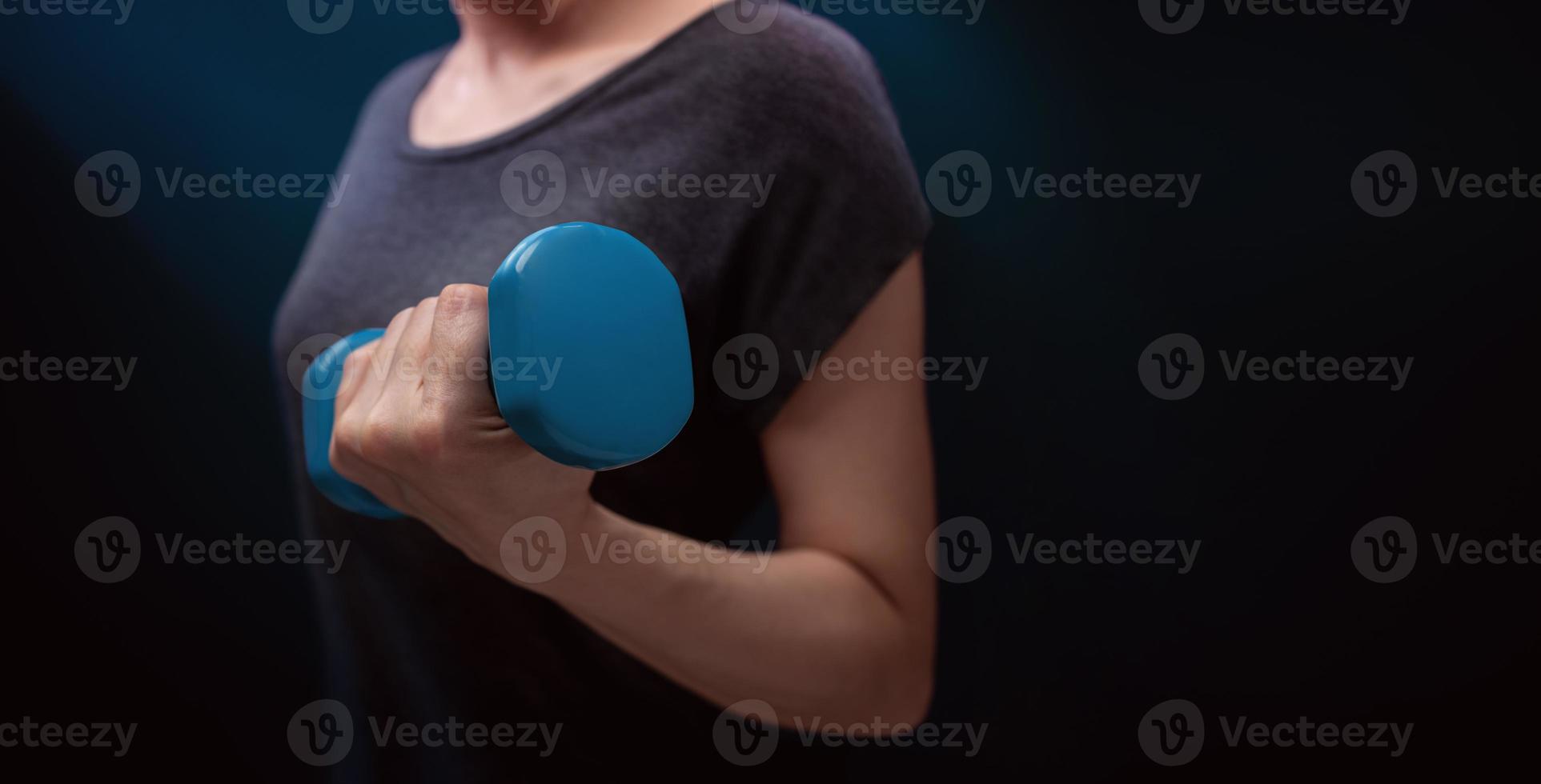 exercice, entraînement avec haltère. concept de sport et de loisirs. gros plan de femme avec haltère bleu dans une pièce sombre à la maison ou à la salle de sport photo