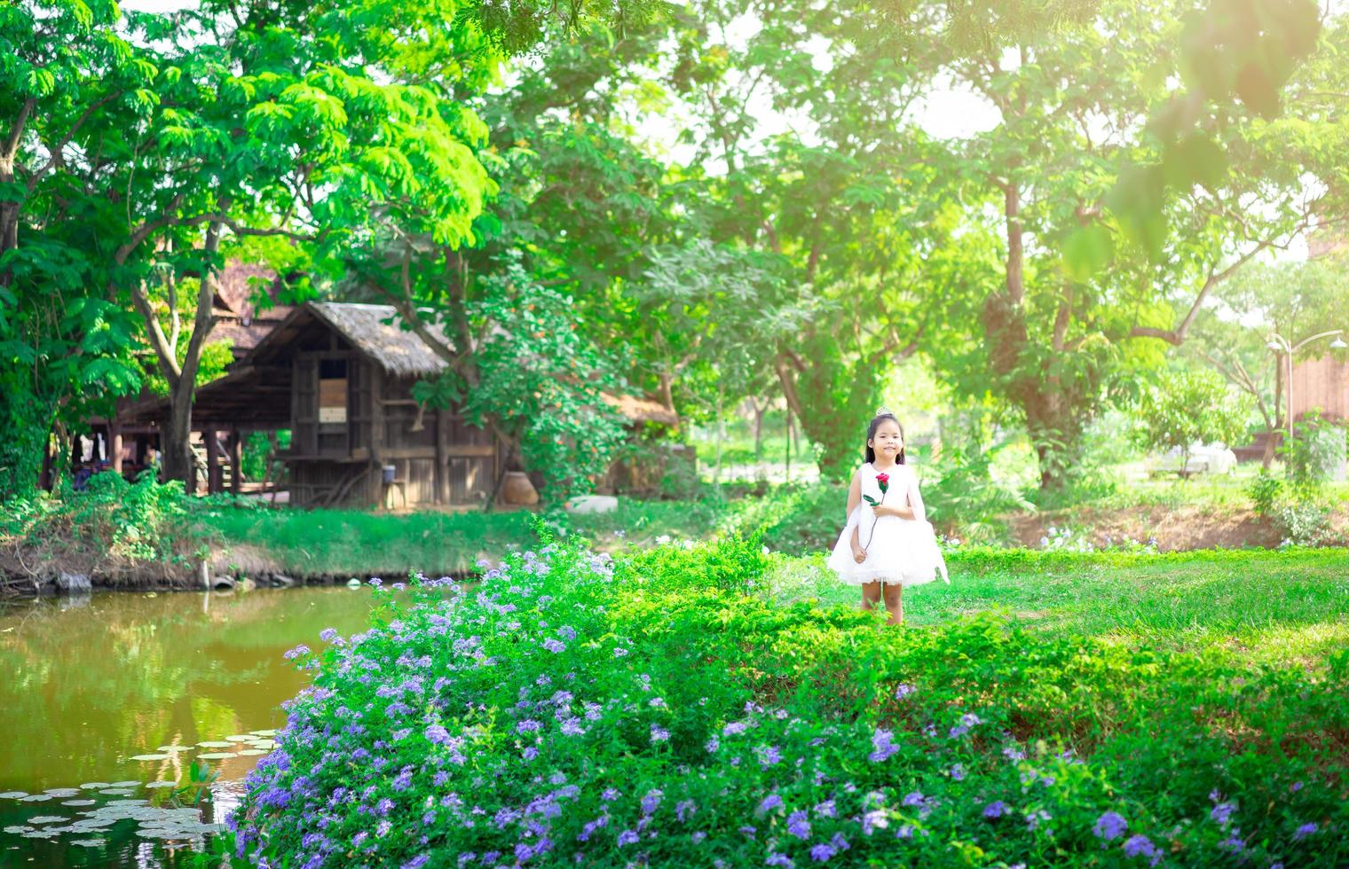 Jolie petite fille asiatique dans une robe blanche debout et tenant une rose rouge dans le parc photo