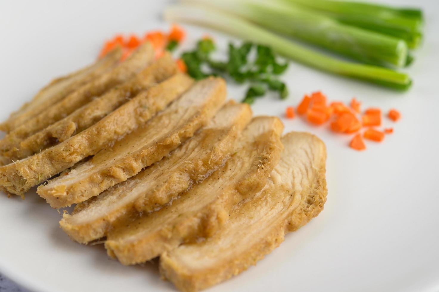 poitrine de poulet cuite à la vapeur sur une assiette blanche avec oignons de printemps et carottes photo