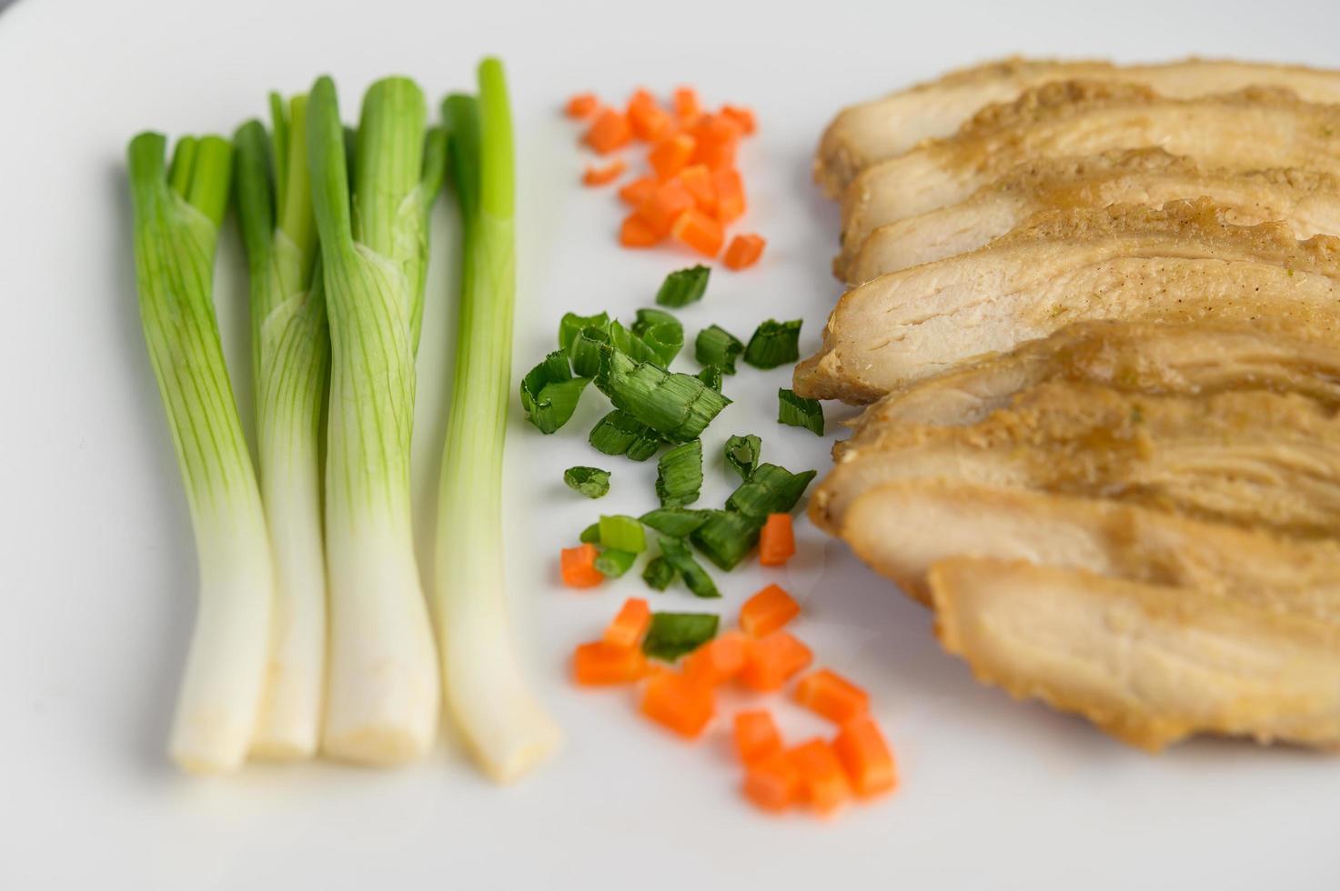 poitrine de poulet cuite à la vapeur sur une assiette blanche avec oignons de printemps et carottes photo