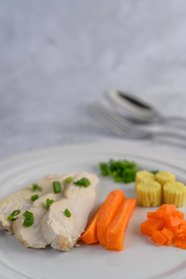 poitrine de poulet cuite à la vapeur sur une assiette blanche avec oignons nouveaux, maïs et carottes photo