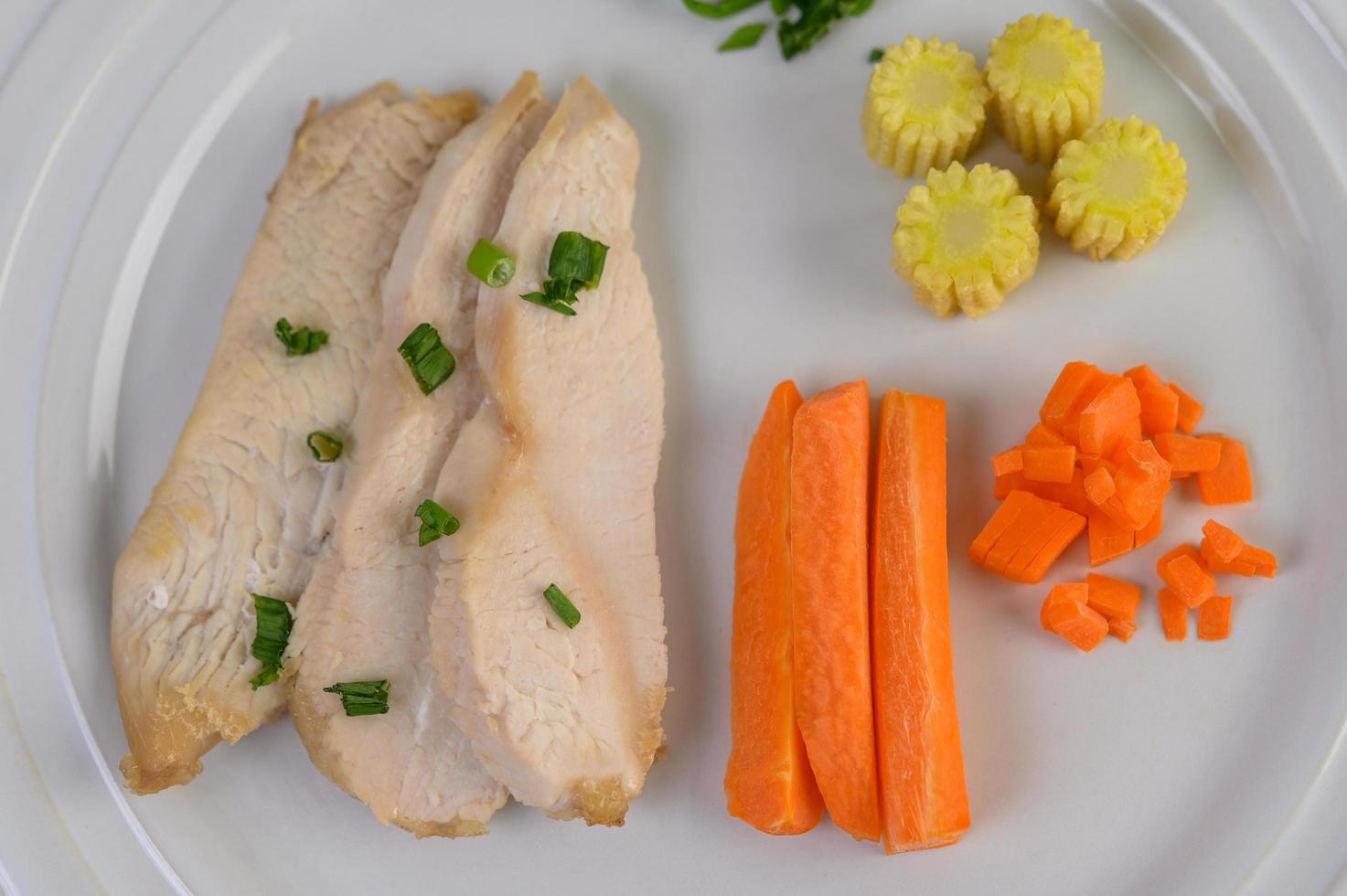 poitrine de poulet cuite à la vapeur sur une assiette blanche avec oignons de printemps et carottes photo