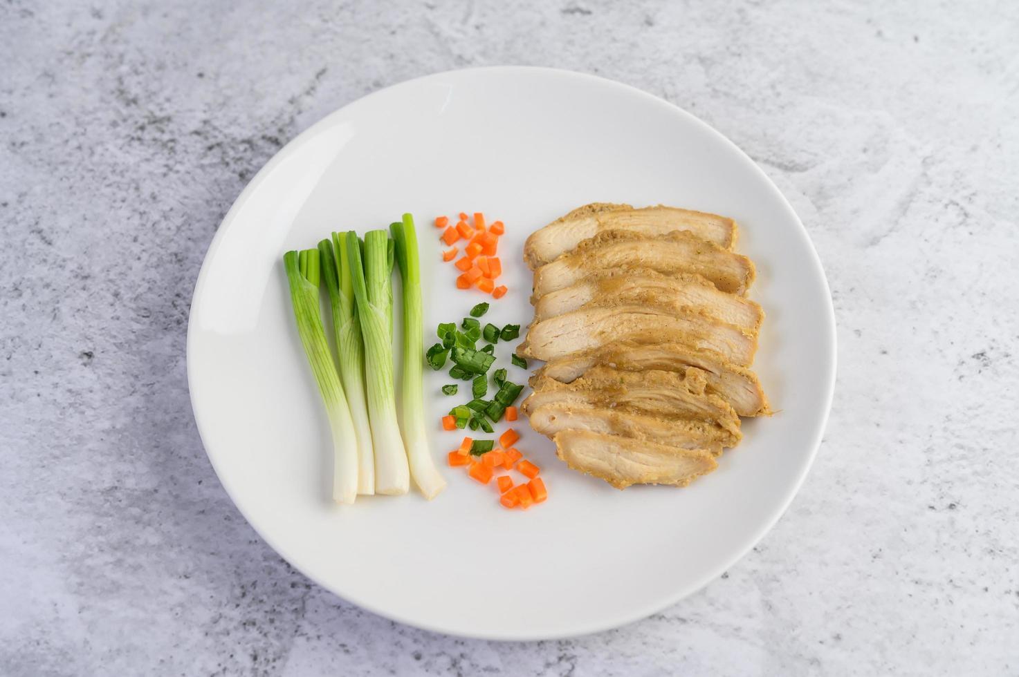 poitrine de poulet cuite à la vapeur sur une assiette blanche avec oignons de printemps et carottes photo