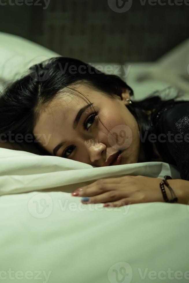 une belle femme asiatique dormant sur une couverture blanche et un oreiller avec des robes noires photo