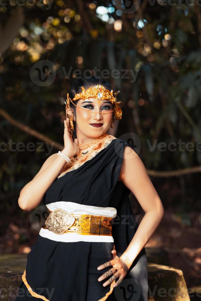 femme asiatique debout et posant avec sa main dans un costume noir tout en portant une couronne dorée et une ceinture dorée sur son corps photo