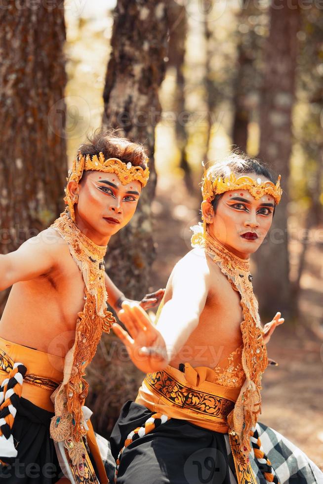 deux hommes balinais dansant ensemble devant l'arbre tout en portant une couronne dorée et des colliers dorés en vêtements dépouillés photo