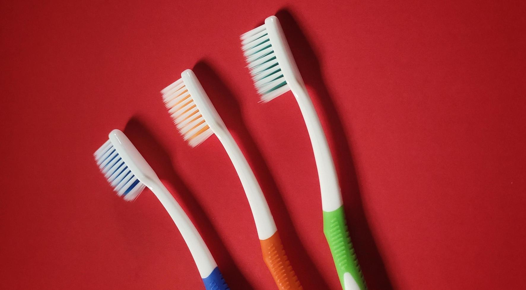 3 brosses à dents de couleurs différentes isolées sur fond rouge photo