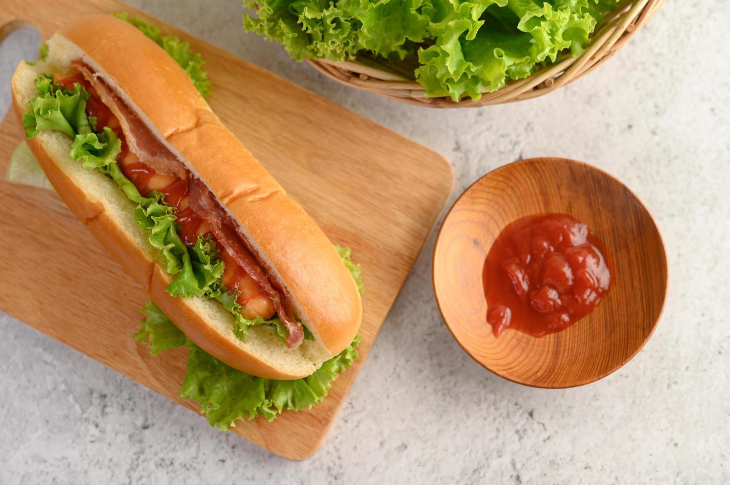 Hot-dog avec laitue et tomate sur une planche à découper en bois photo