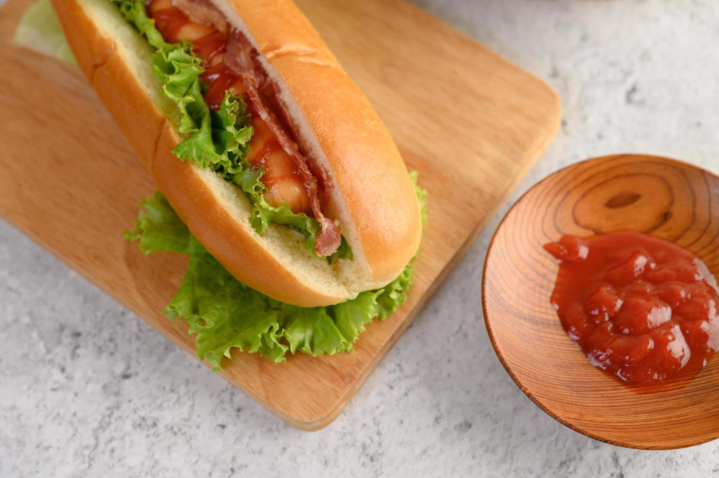 Hot-dog avec laitue et tomate sur une planche à découper en bois photo