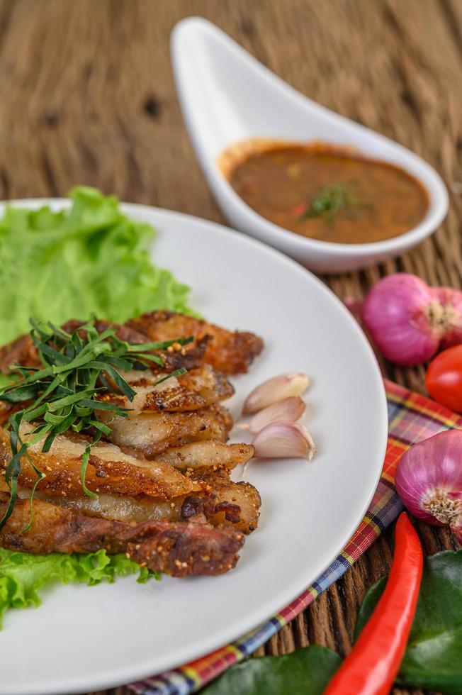 Cou de porc grillé sur une plaque blanche avec oignon rouge, tomate et piment sur une table en bois photo