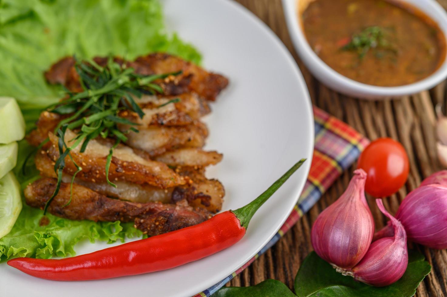 Cou de porc grillé sur une plaque blanche avec oignon rouge, tomate et piment sur une table en bois photo