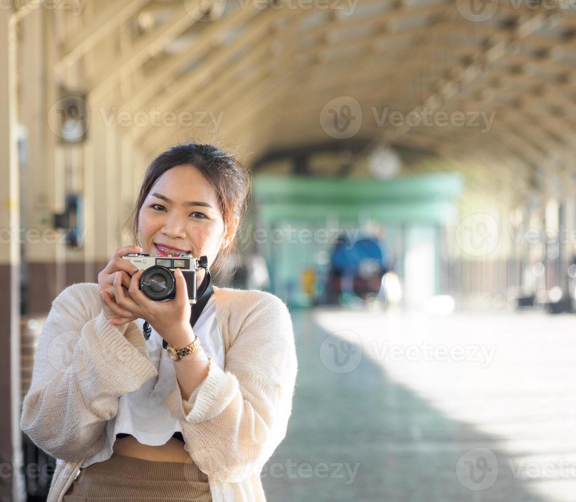 yong girl asian woman beautiful cool long hair wearing white shirt model with retro film camera standing at train station bangkok, travel on vacation pendant la soirée photo