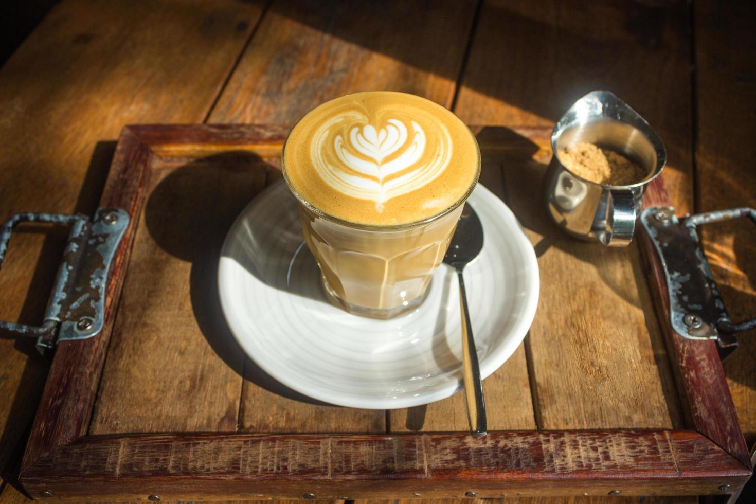 Café avec art latte sur plaque blanche et plateau en bois au soleil photo