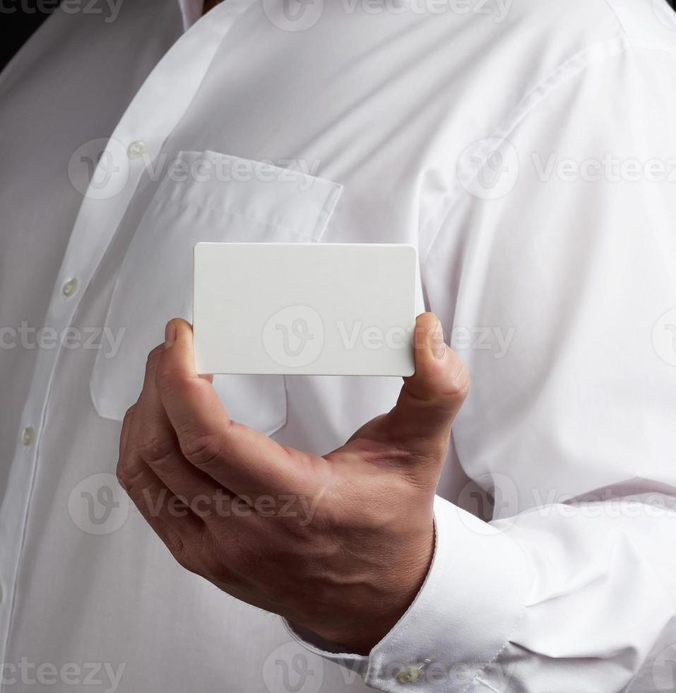 la main masculine tient une carte de visite rectangulaire en papier blanc vide photo