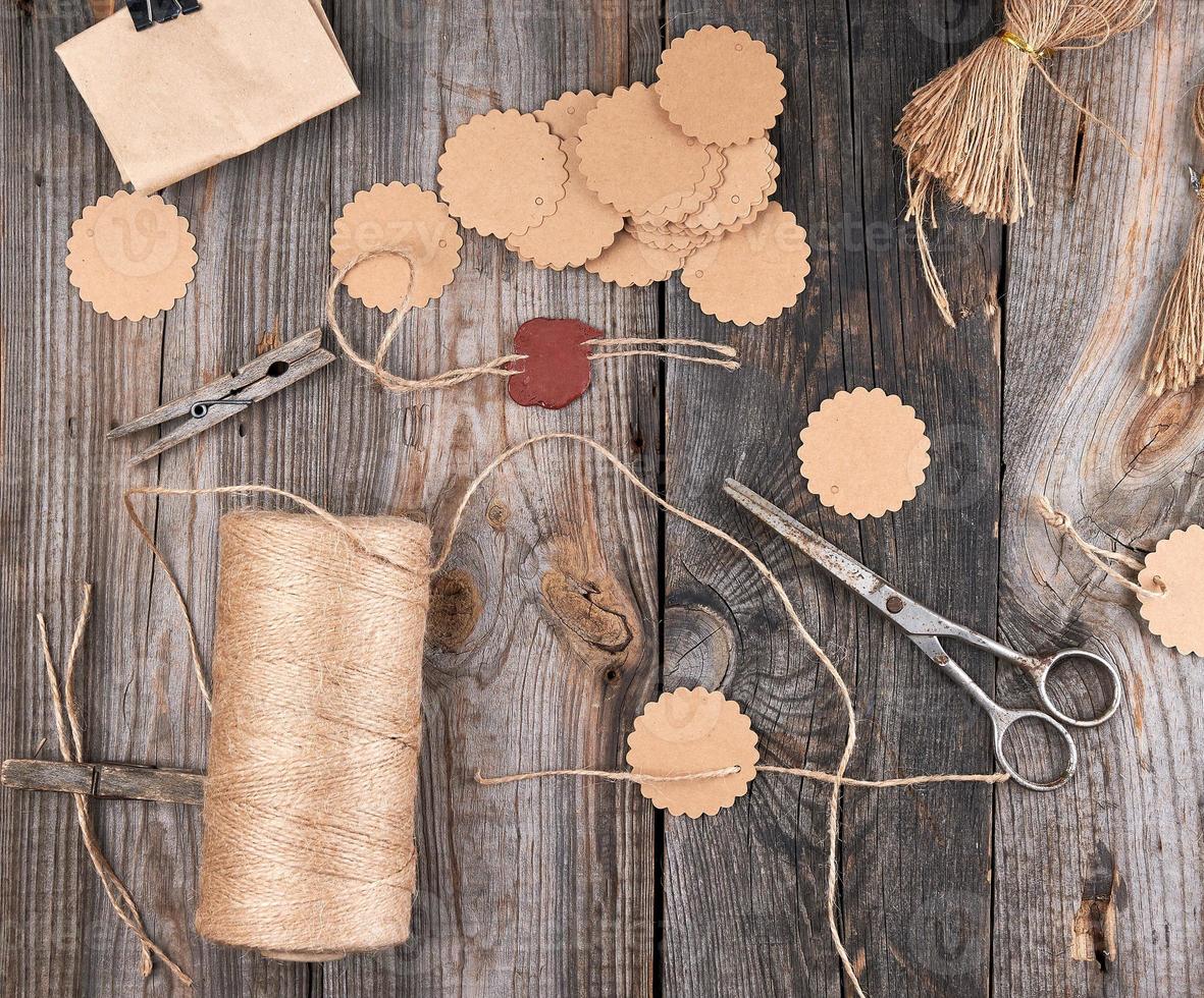 une bobine de corde marron, des étiquettes en papier et de vieux ciseaux sur un fond de bois gris photo