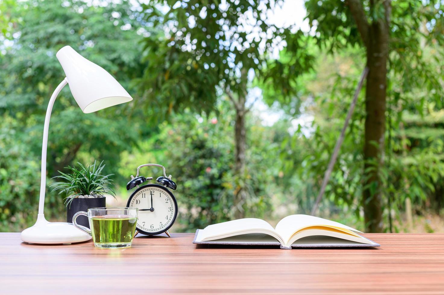 livre avec horloge, thé et lampe sur un bureau à l'extérieur photo