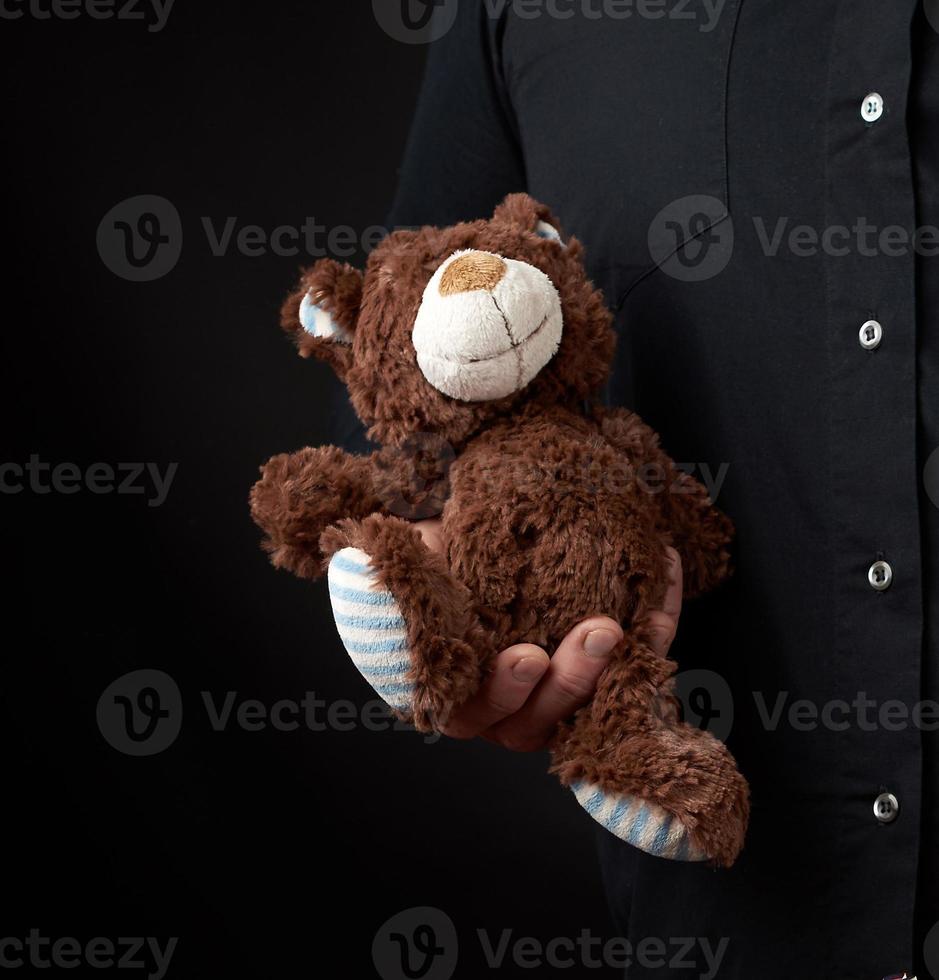 homme adulte dans une chemise noire tient un ours en peluche brun sur fond sombre photo