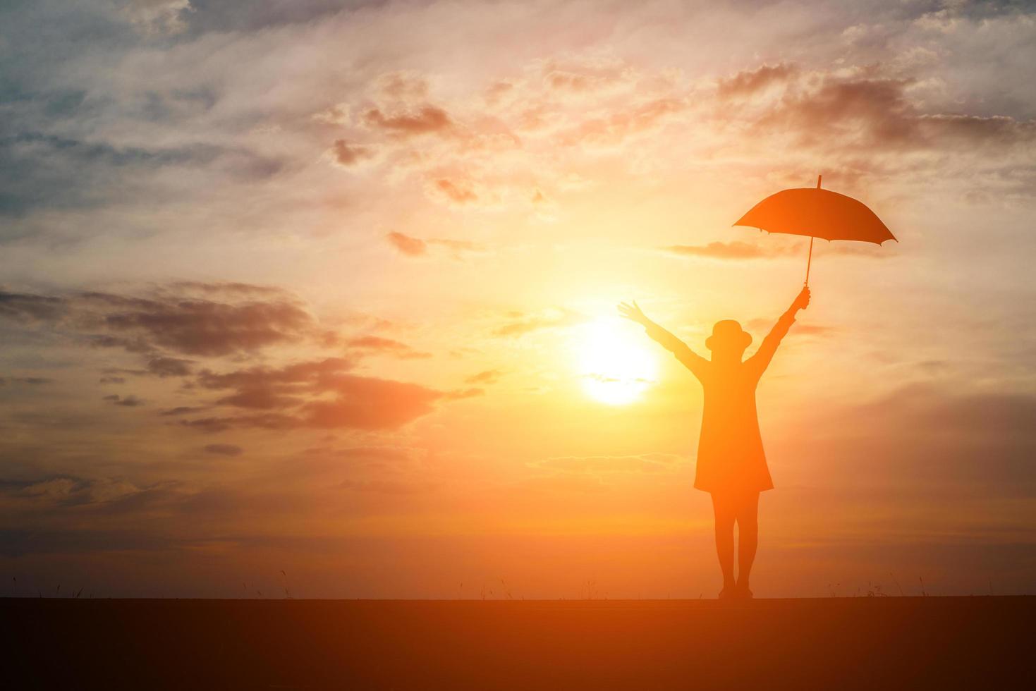 silhouette d'une femme tenant un parapluie sur la plage et le coucher du soleil photo