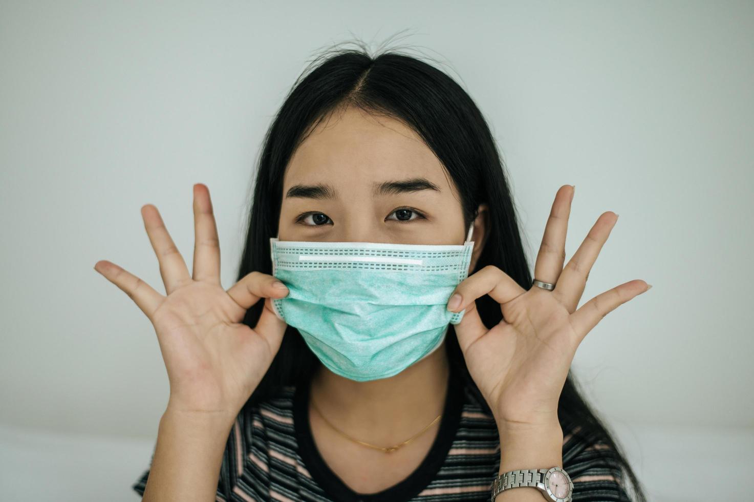 fille portant un masque sanitaire, une chemise rayée et un symbole de main ok photo