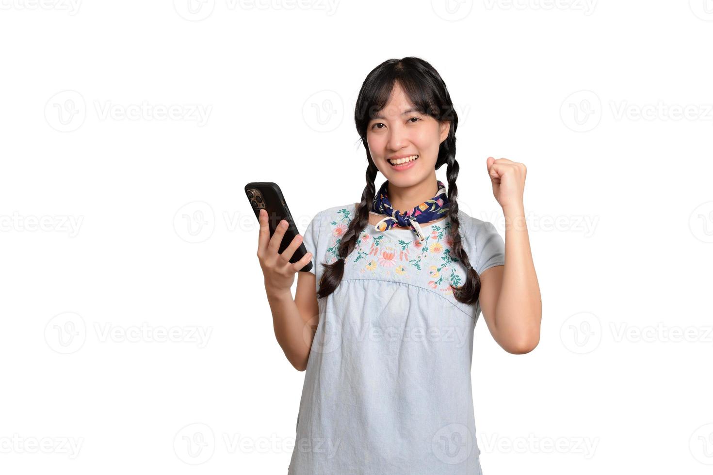 portrait d'heureuse belle jeune femme asiatique en robe denim à l'aide d'un smartphone sur fond blanc. tourné en studio photo
