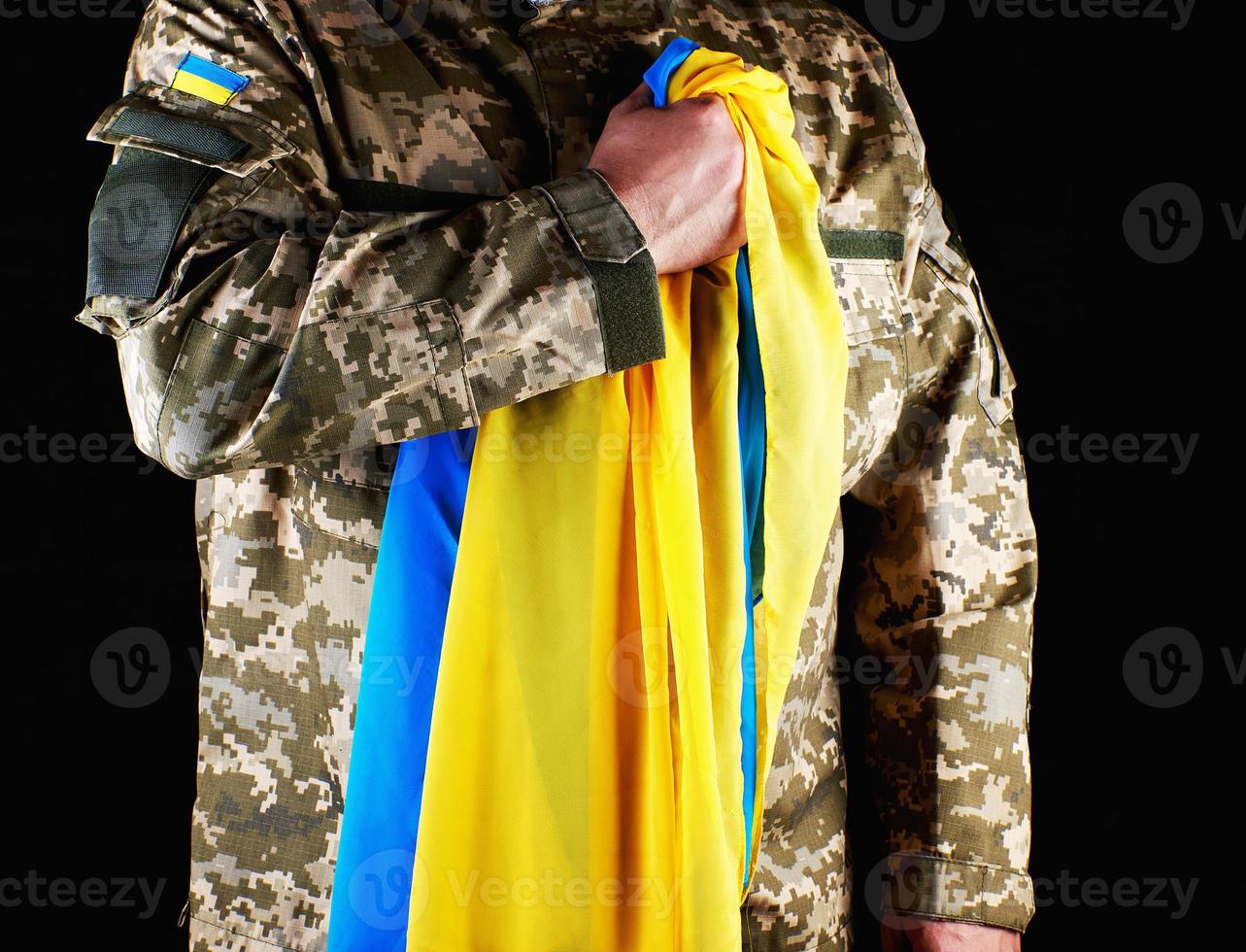 soldat ukrainien tient dans sa main le drapeau jaune-bleu de l'état, il a appuyé sa main sur sa poitrine photo