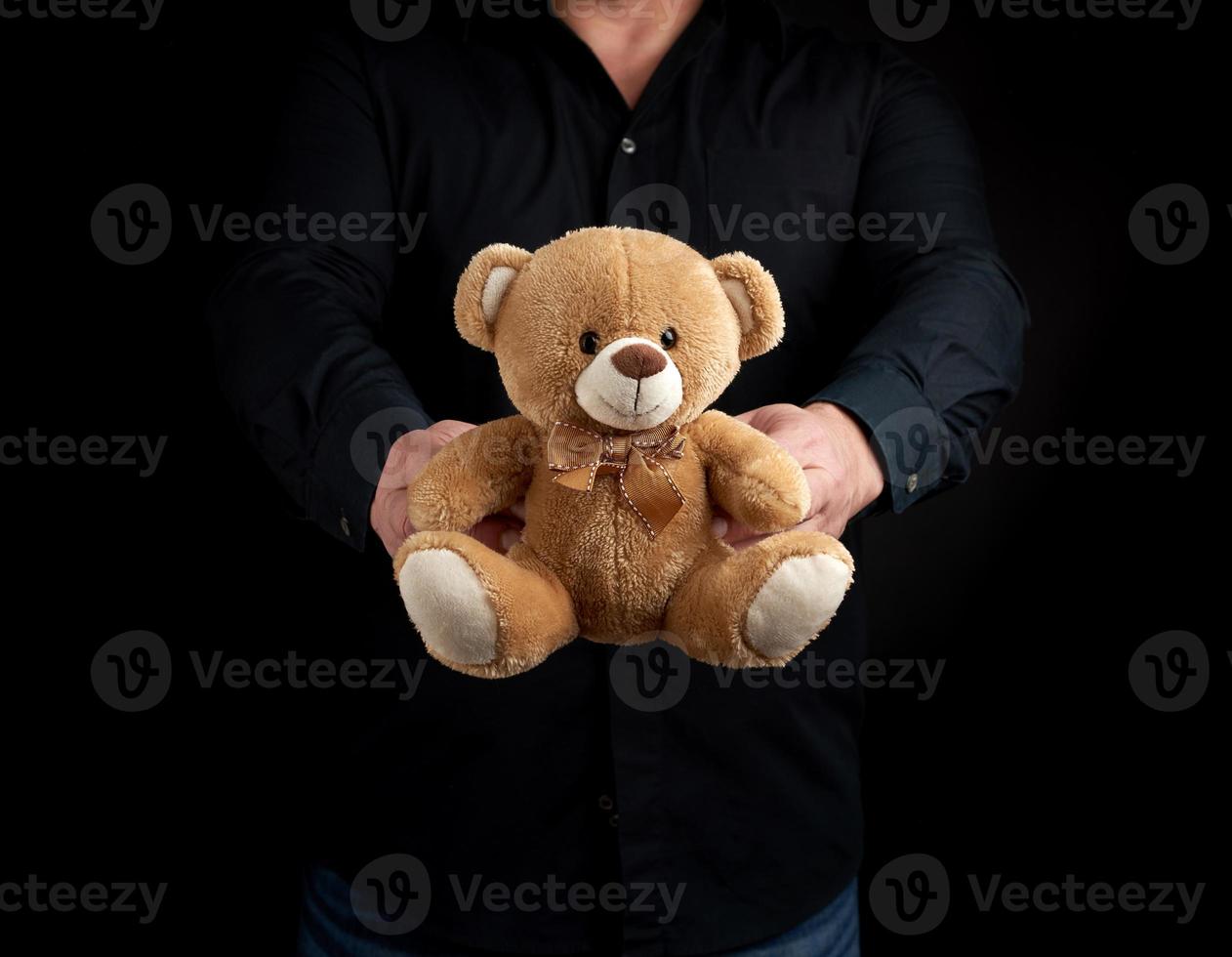 homme adulte dans une chemise noire tient un ours en peluche brun