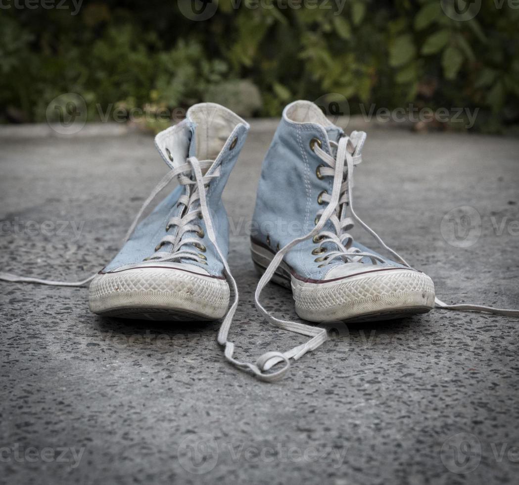 Paire de vieilles baskets en textile bleu usé sur asphalte gris photo