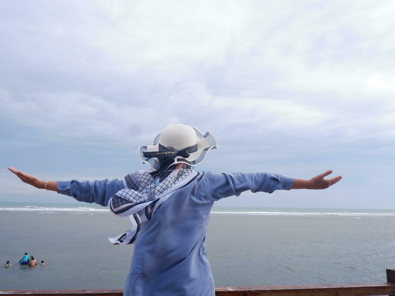 dos de la femme au chapeau sur la plage tropicale qui regardait le ciel et la mer tout en étendant ses mains sur le pont. vue sur la mer photo