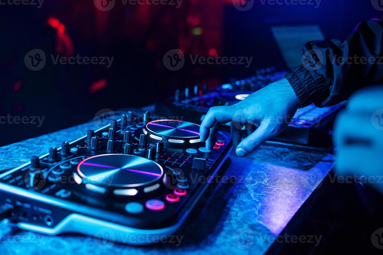 console dj pour mixer de la musique avec les mains et avec des personnes floues dansant lors d'une soirée en boîte de nuit photo