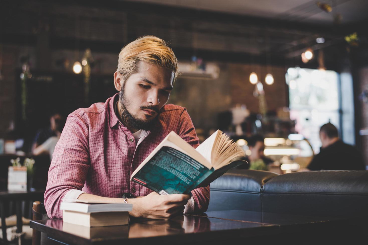 Jeune hipster barbu lisant un livre dans un café photo