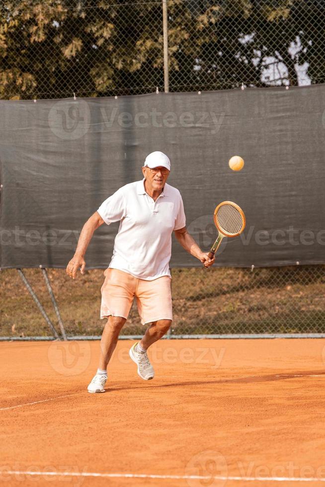 joueur de tennis senior vêtu de vêtements de sport en action sur un court de tennis en terre battue photo