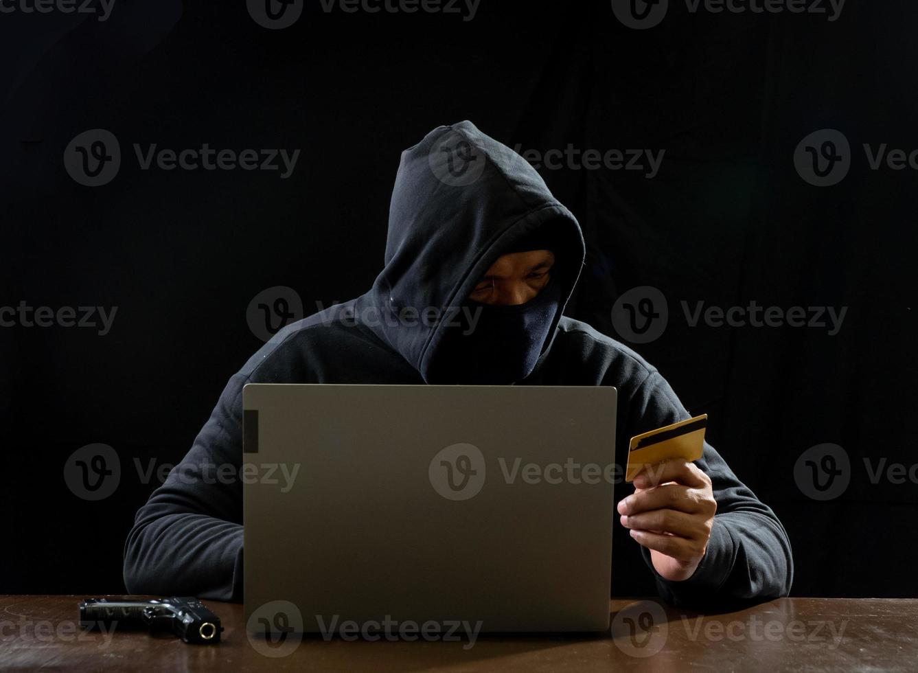 pirate espion homme une personne en sweat à capuche noir assis sur une table à la recherche d'un ordinateur portable utilisé la sécurité d'attaque par mot de passe de connexion pour faire circuler des données numériques dans le système de réseau Internet, fond sombre de nuit. photo