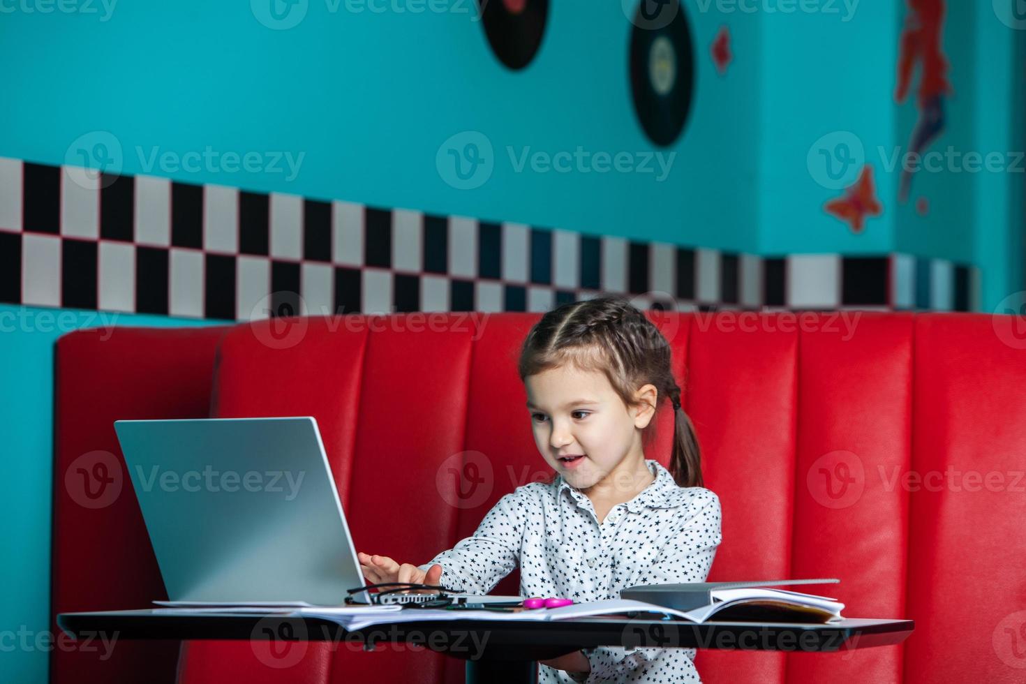 jolie petite fille utilisant un ordinateur portable à la maison. concept de retour à l'école. la fille fait ses devoirs seule sur l'ordinateur portable photo