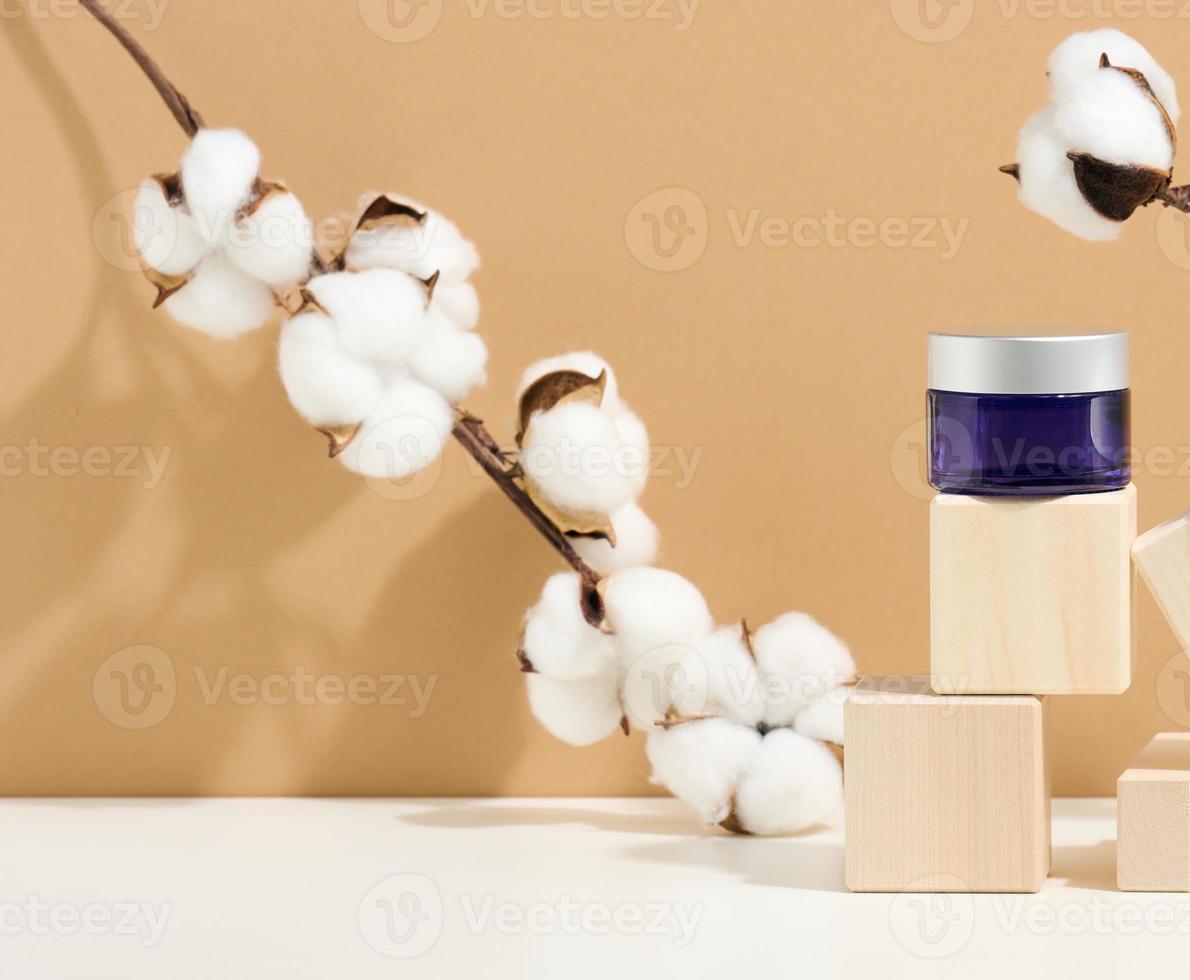 les produits cosmétiques dans un bocal en verre bleu avec un couvercle gris se tiennent sur un podium en bois fait de cubes. vierge pour les produits de marque, hydratant sur fond beige photo