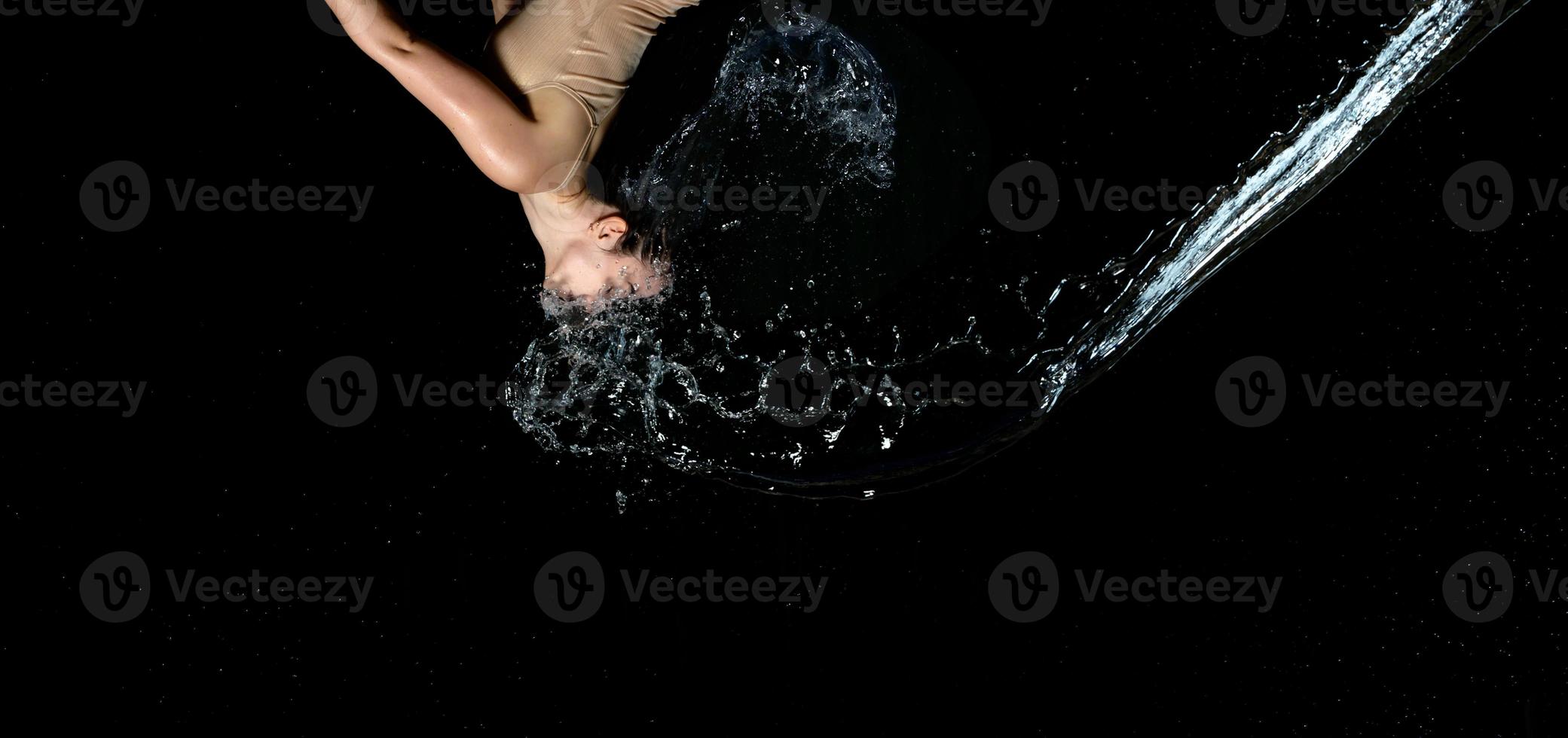 belle femme d'apparence caucasienne aux cheveux noirs en gouttes d'eau sur fond noir photo