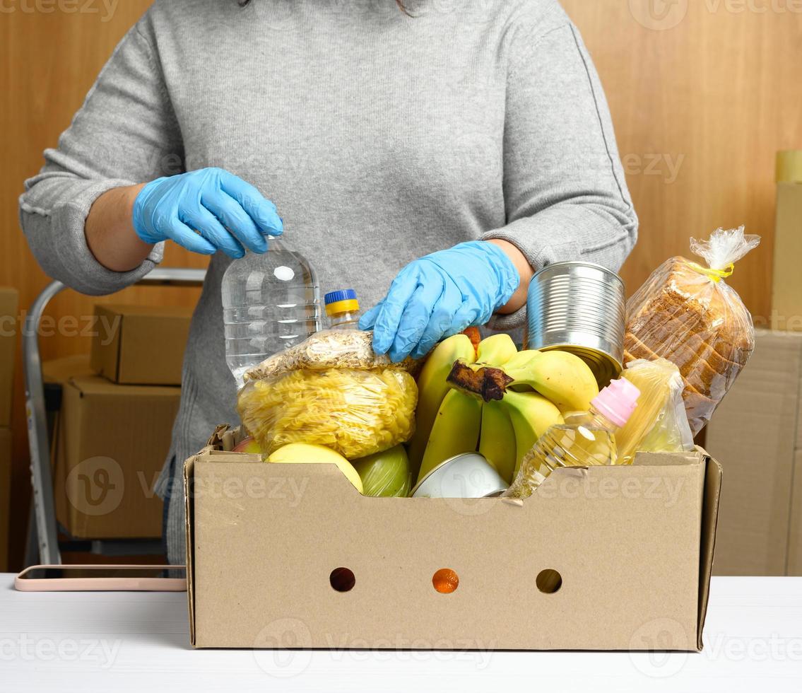 une femme en gants continue de collecter de la nourriture, des fruits et des objets et une boîte en carton pour aider ceux qui en ont besoin photo