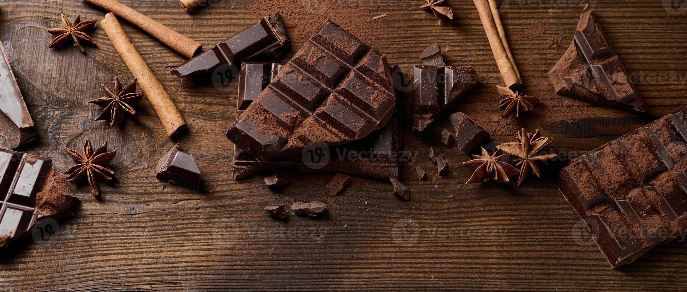 morceaux cassés de chocolat noir, bâtons de cannelle et anis étoilé sur une table en bois marron, vue de dessus photo