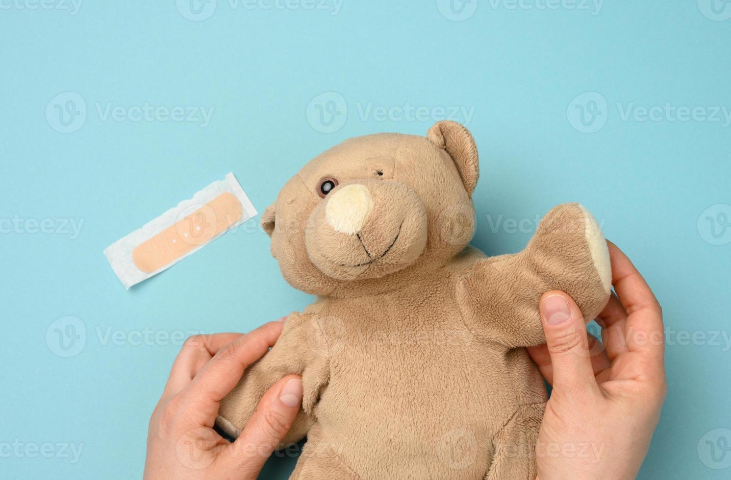main de femme tenant un ours en peluche brun avec un œil arraché sur fond bleu photo