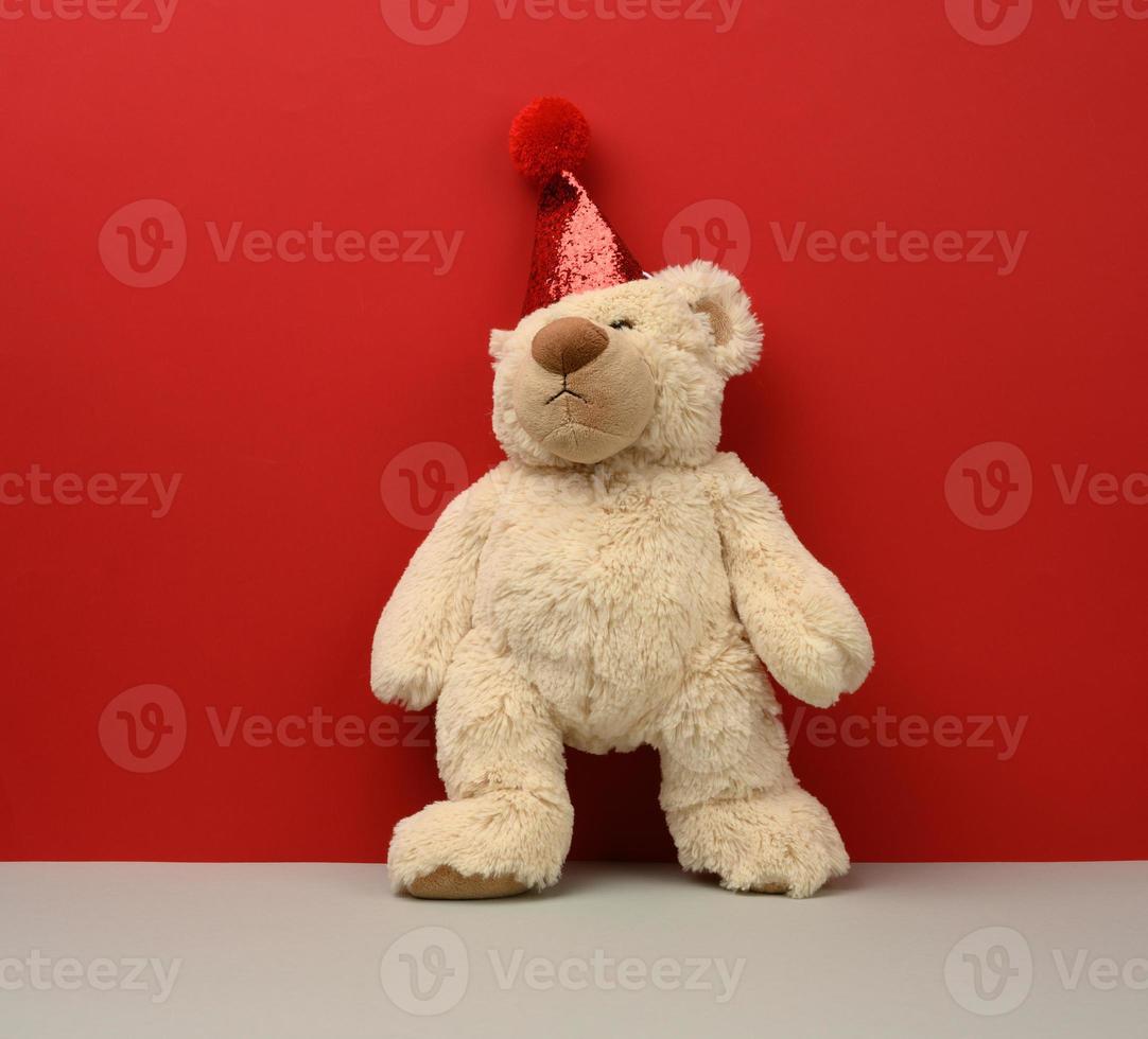 ours en peluche beige dans un bonnet rouge sur fond rouge photo