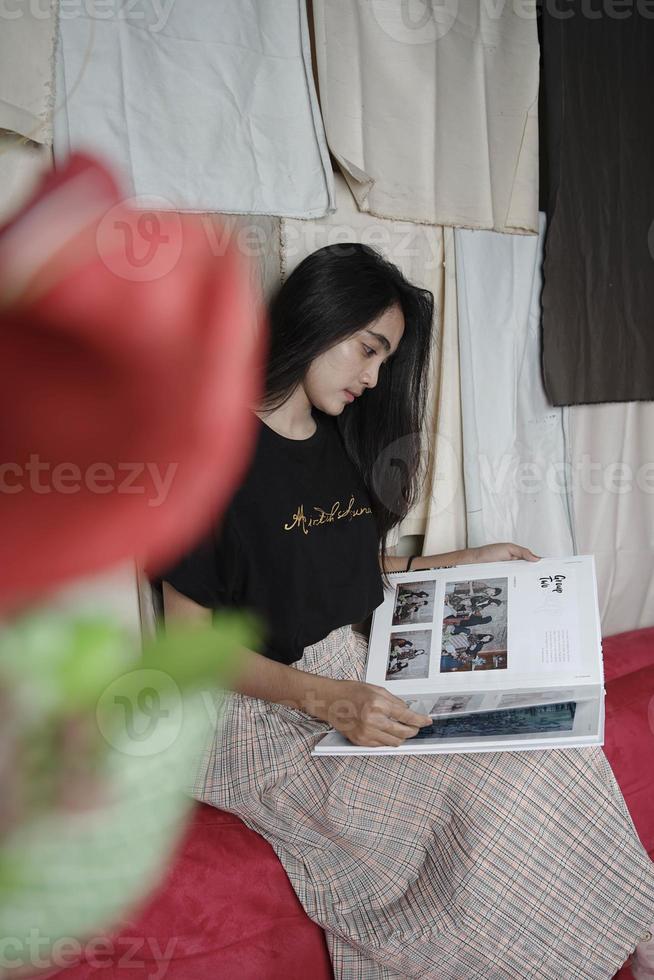 une femme asiatique d'indonésie est assise et lit un livre sur un fond de tissu coloré. photo