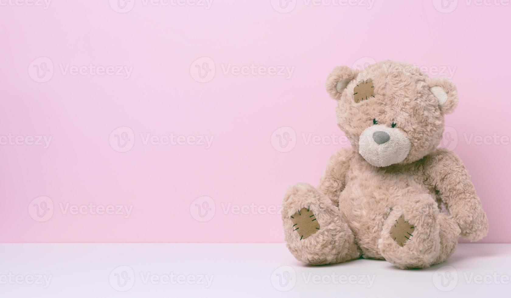 marron nounours ours avec patchs est assis sur une blanc tableau, rose Contexte photo