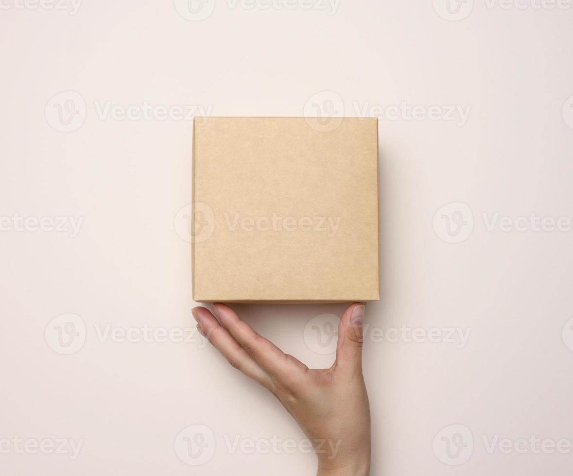 femelle main en portant une carré papier carton boîte sur une beige Contexte photo