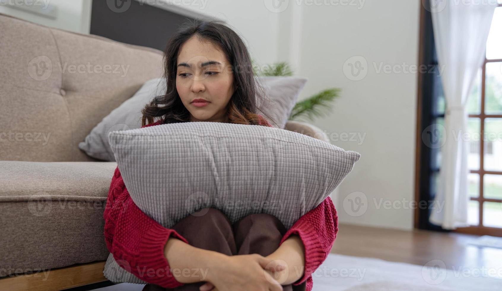 Malheureuse jolie jeune femme asiatique assise seule sur un canapé avec un sentiment de tristesse photo