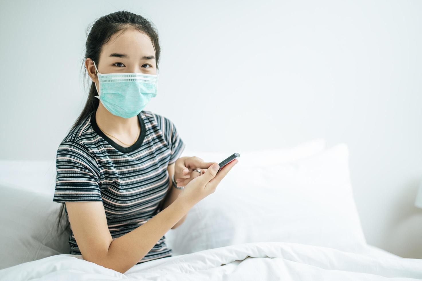 fille portant un masque sanitaire, chemise rayée et tenant un téléphone portable photo