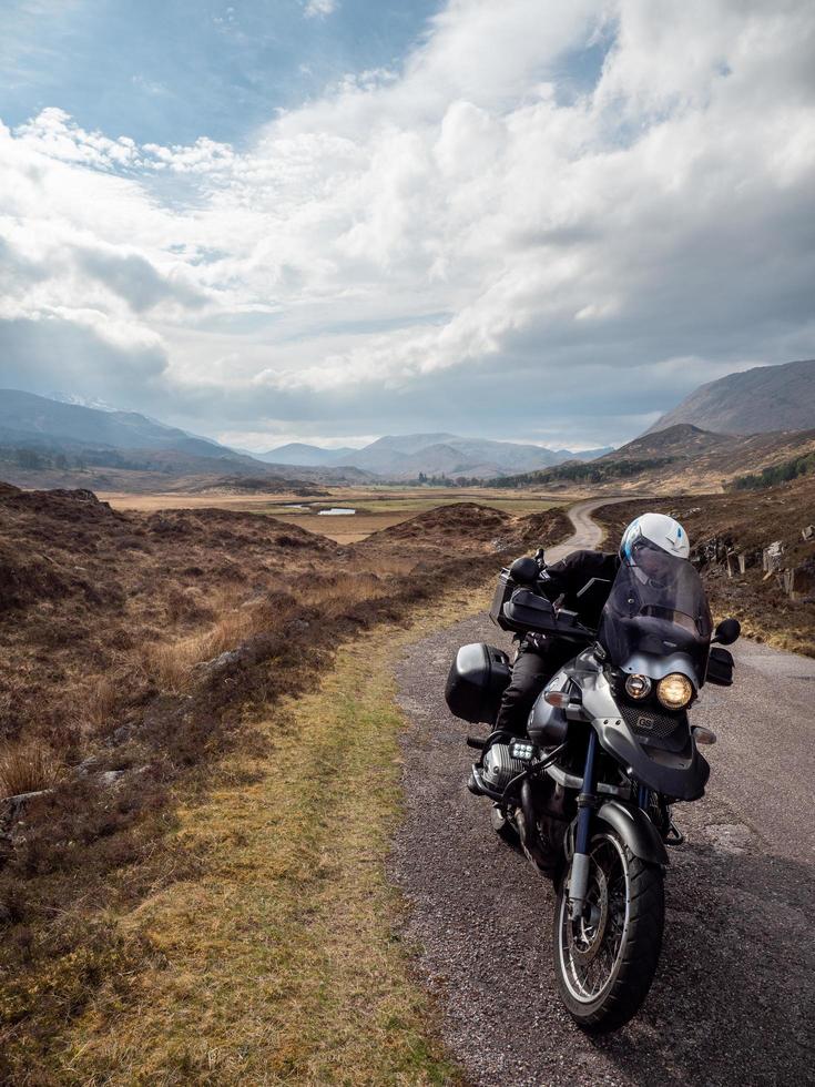 Personne en moto avec des montagnes et un ciel bleu nuageux en Ecosse photo