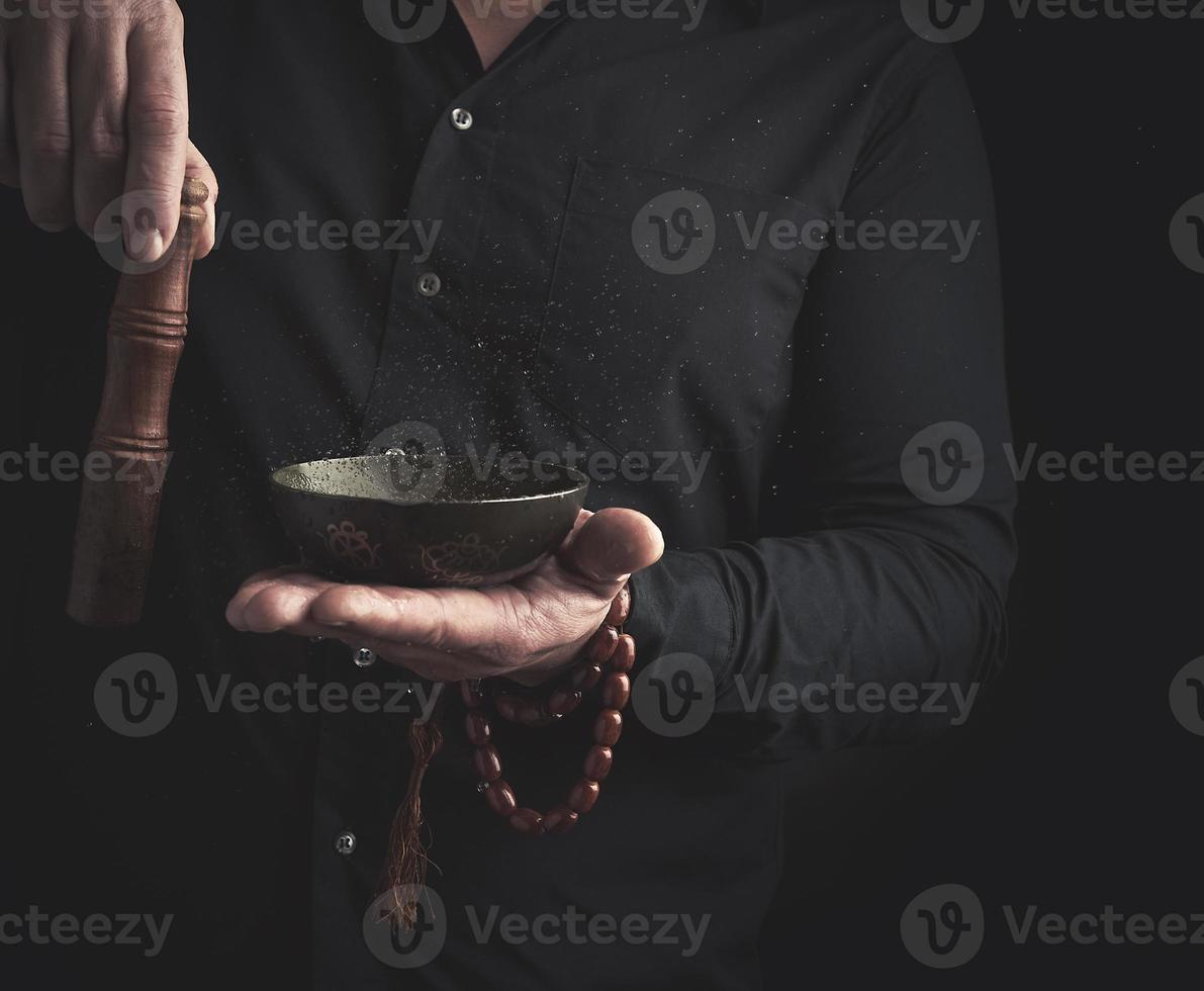 homme dans une noir chemise tourne une en bois bâton autour une cuivre Tibétain bol de l'eau. rituel de méditation photo