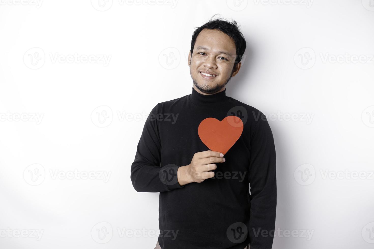 une portrait de une content asiatique homme portant une noir chemise, en portant une rouge en forme de coeur papier isolé par blanc Contexte photo