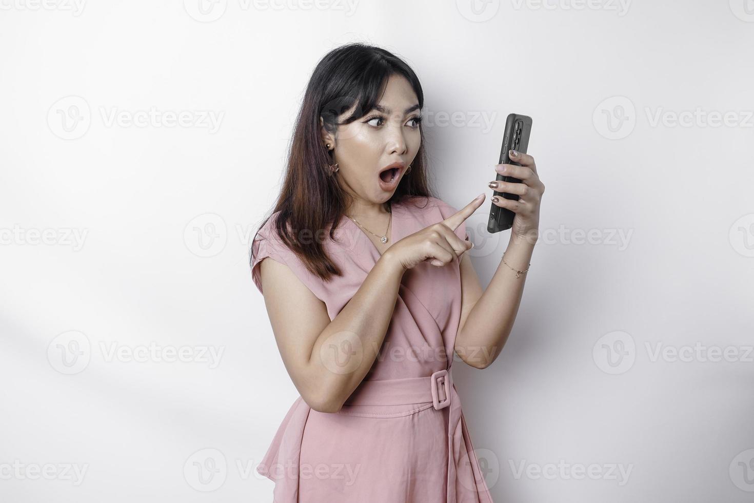 sous le choc asiatique femme habillé dans rose et en portant sa téléphone, isolé par blanc Contexte photo