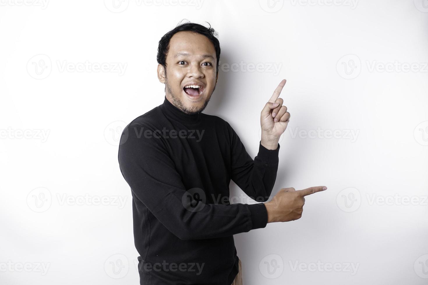 excité asiatique homme portant noir chemise montrer du doigt à le copie espace à côté de lui, isolé par blanc Contexte photo