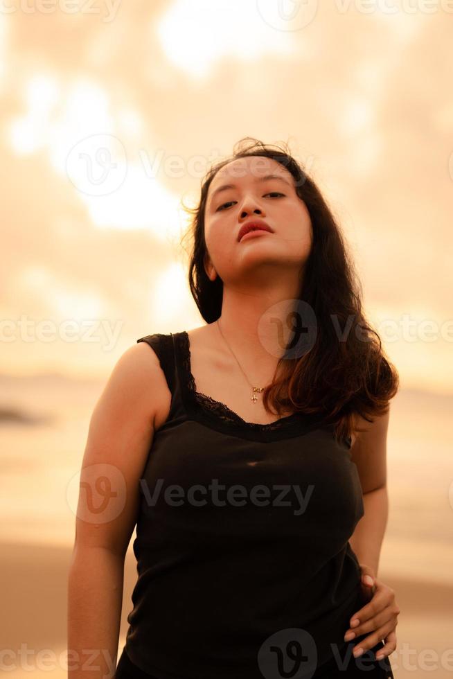 portrait image de un asiatique femme avec noir cheveux et un en colère expression permanent sur le plage dans sa noir vêtements photo